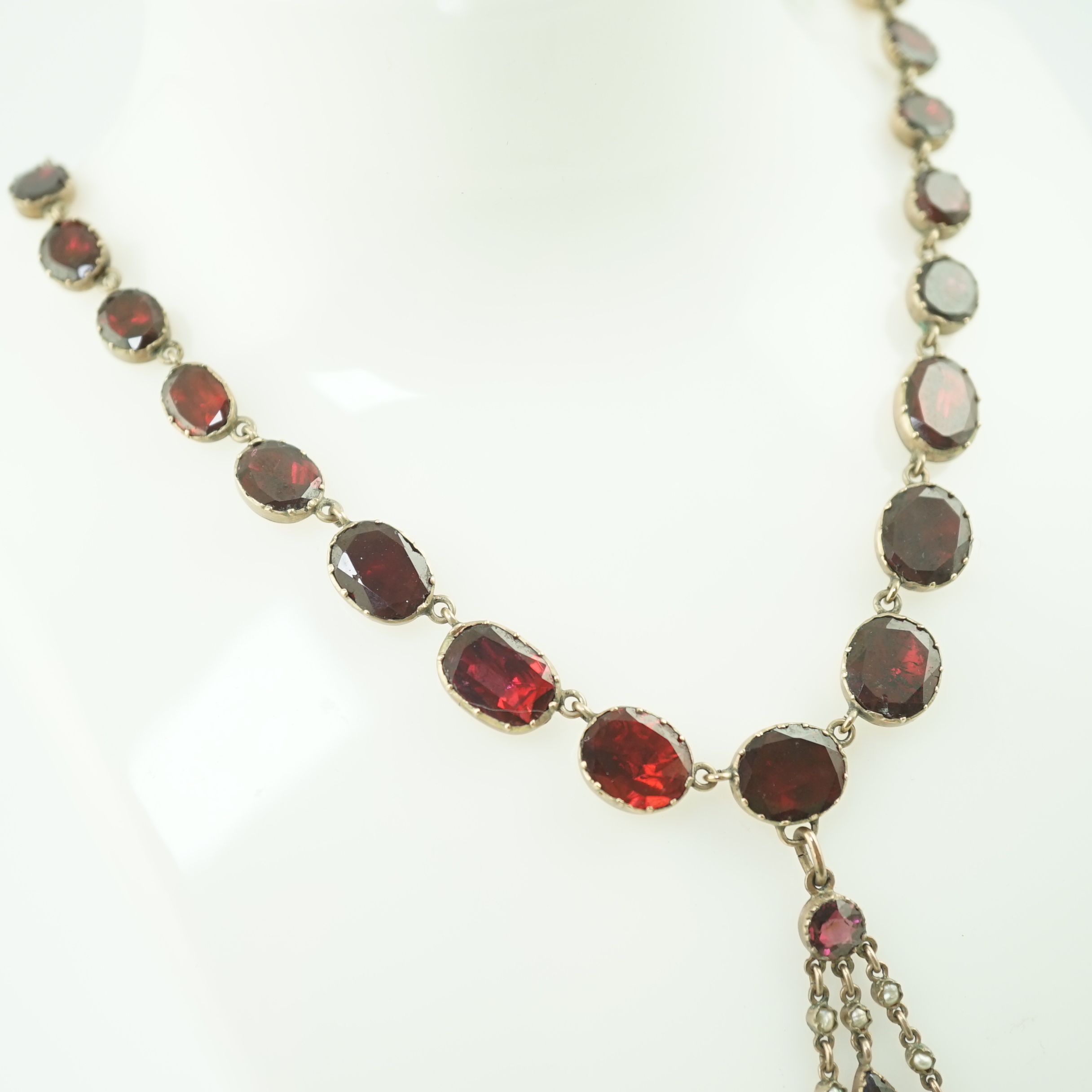 An early 19th century gold, and thirty five graduated foil backed garnet set necklace, with later garnet and seed pearl set drop